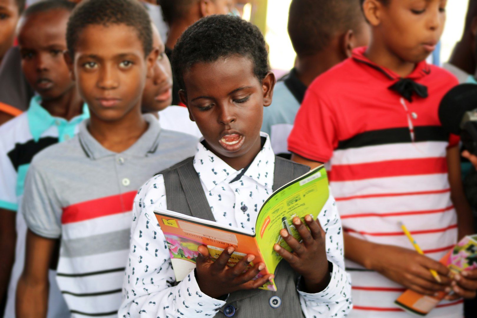 Black man teacher showing group of multiethnic children mushrooms outdoors in park, children sitting on grass attentively observing and listening during educational nature lesson